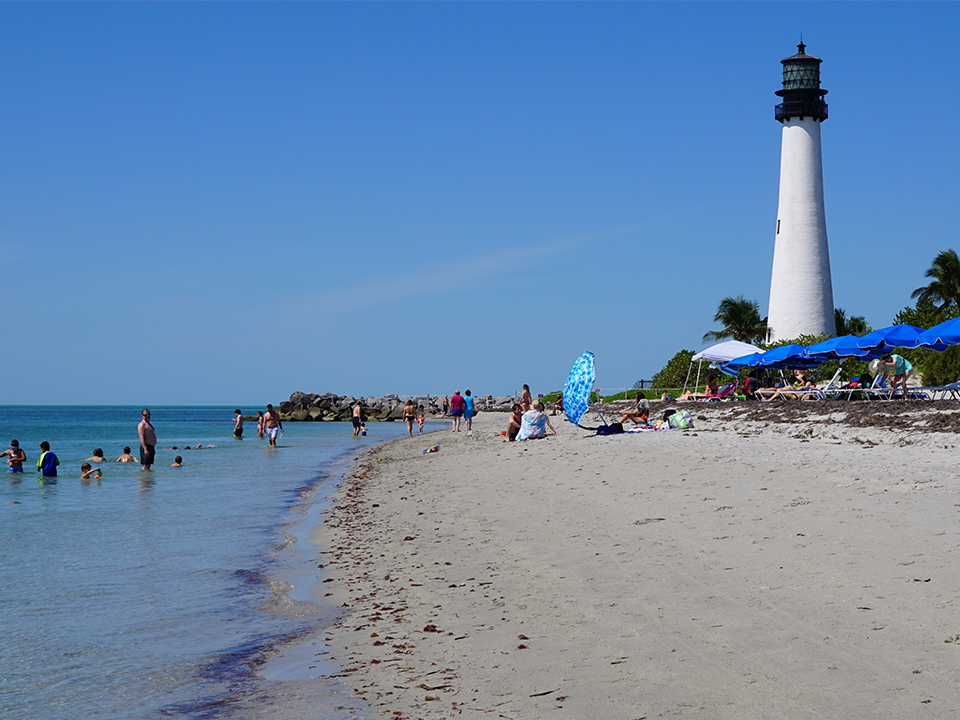 beach goers enjoy the beach with a lighthouse in the background