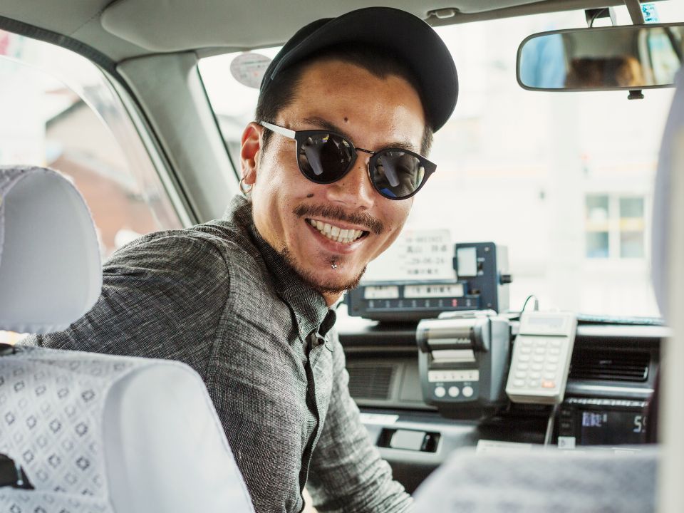 Smiling taxi driver in sunglasses looking back from the driver's seat of his cab