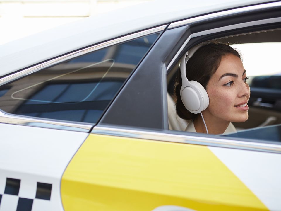 Woman wearing headphones looking out the window from the back seat of a taxi